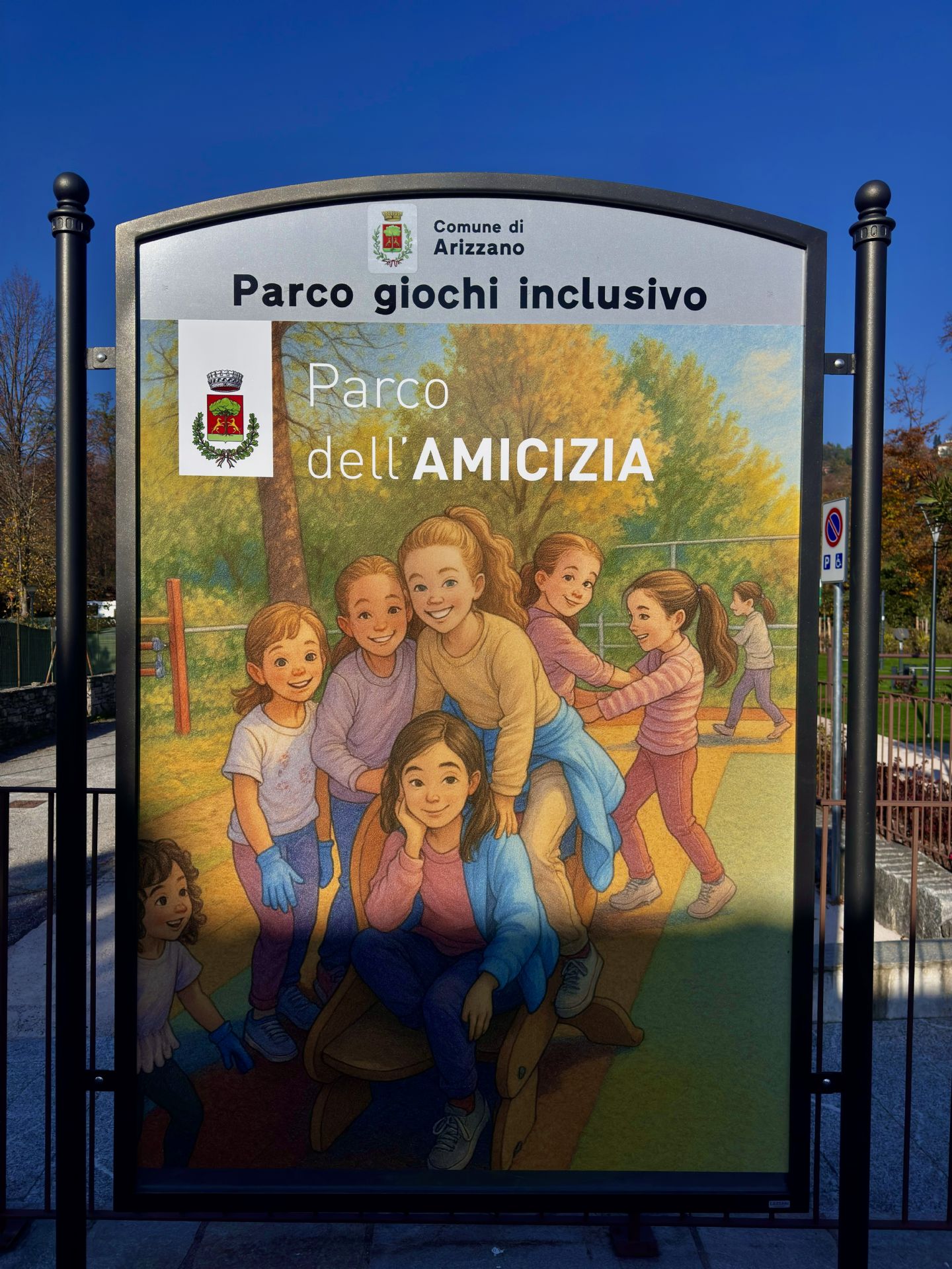 Cartello del Parco giochi inclusivo con nome "Parco dell'Amicizia" e immagine di bambini che giocano effetto cartone animato